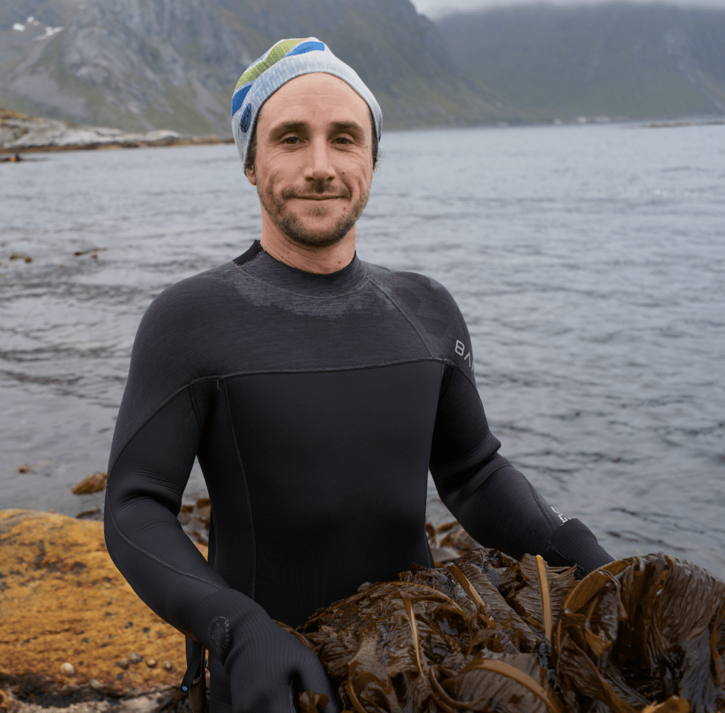 man in wetsuit holding a bucket of kelp