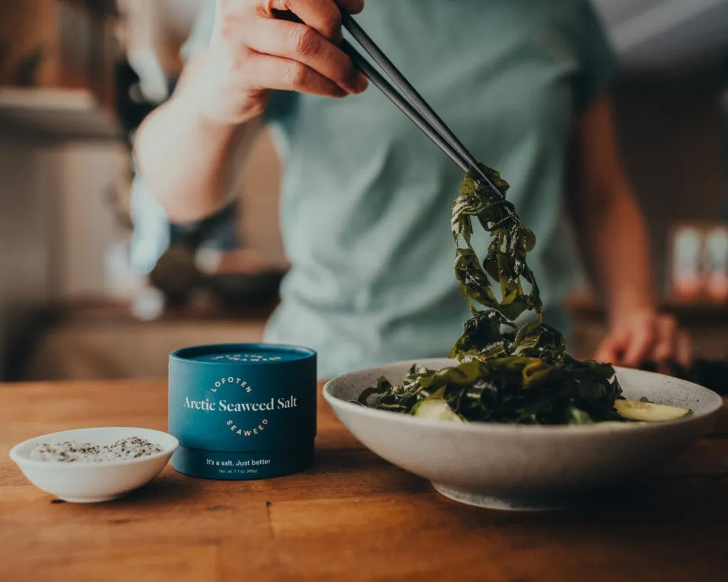 A person holding fresh wakame seaweed in a pair of chopsticks